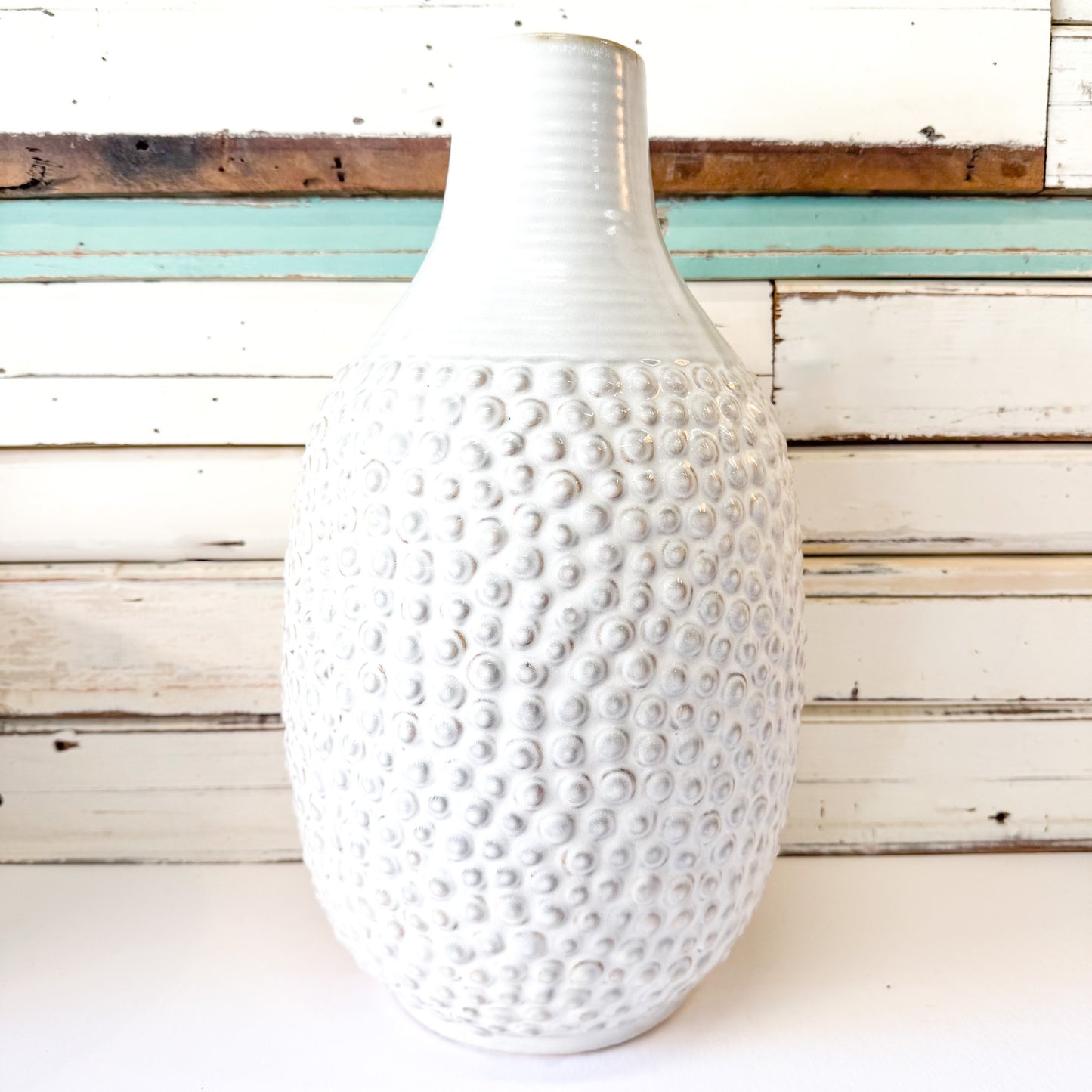 White textured vase on a white surface with a wooden background