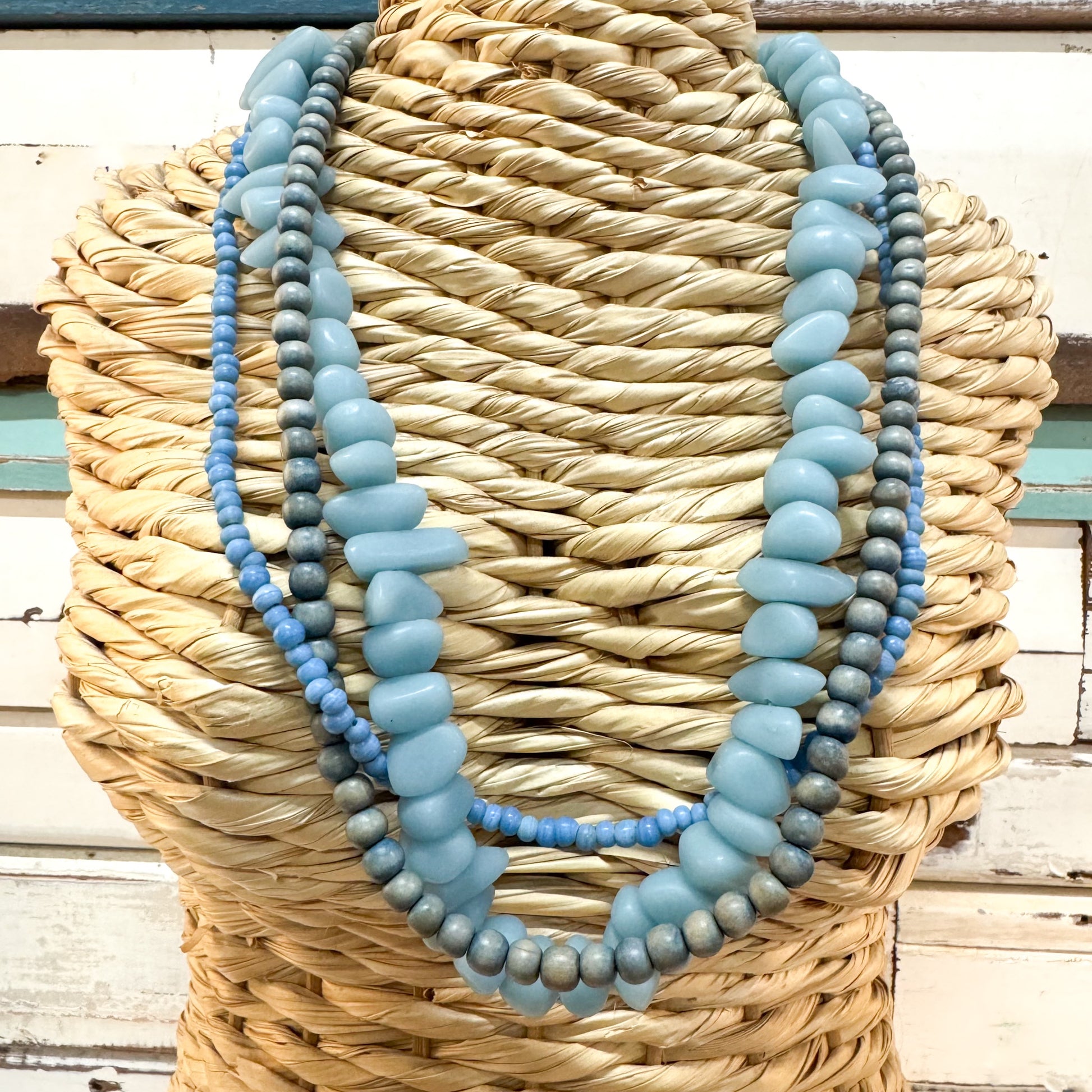 The Brightside Store | Sundaze Necklace ~ Beach Chill
A three-strand beaded necklace displayed on a woven straw mannequin torso. The necklace features light blue chunky oval beads, medium blue round beads, and gray-blue oval beads.