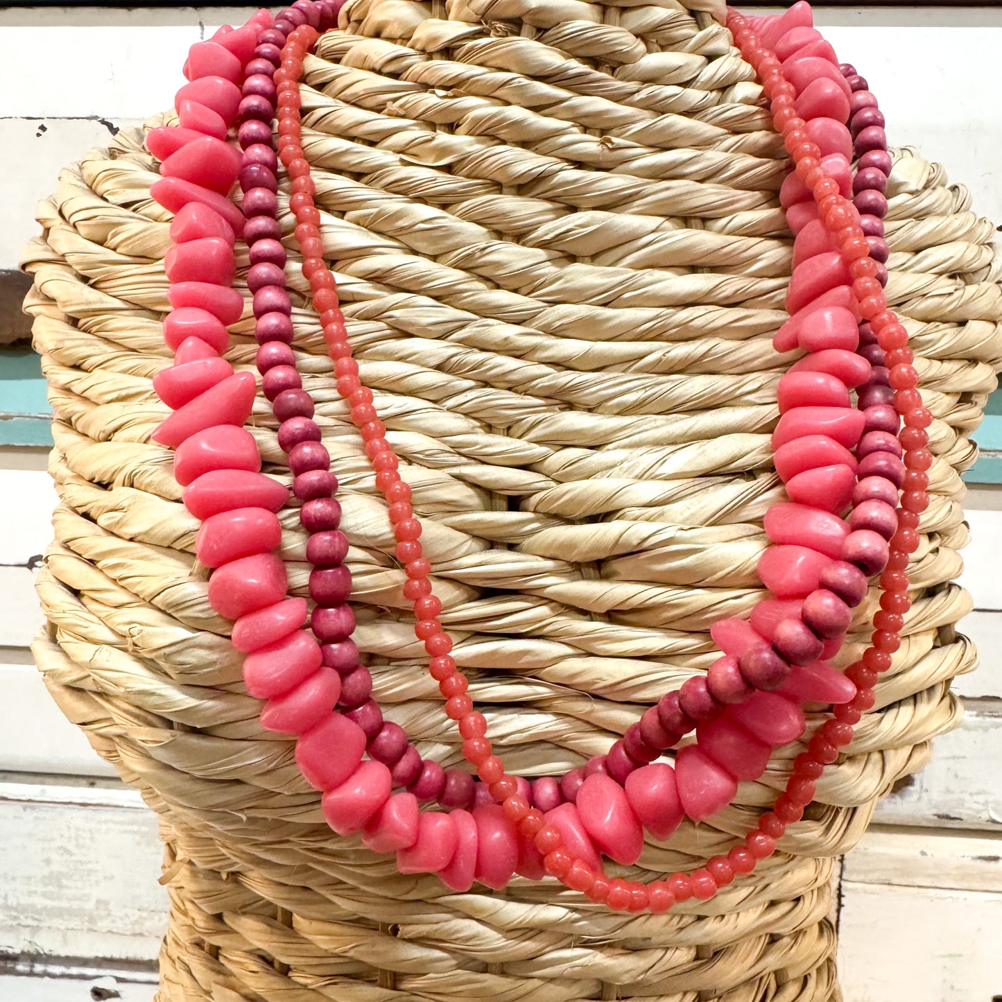 The Brightside Store | Sundaze Necklace ~ Sundowner Three layered beaded necklaces in shades of pink, coral, and deep magenta, draped over a woven straw mannequin head.