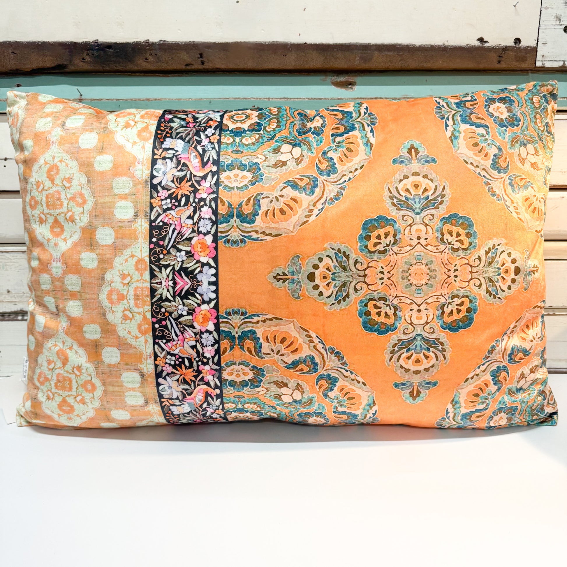 A square decorative throw pillow with a vibrant orange background and intricate multicolor patterns, featuring a central vertical panel with floral motifs and a larger medallion pattern on the right side.