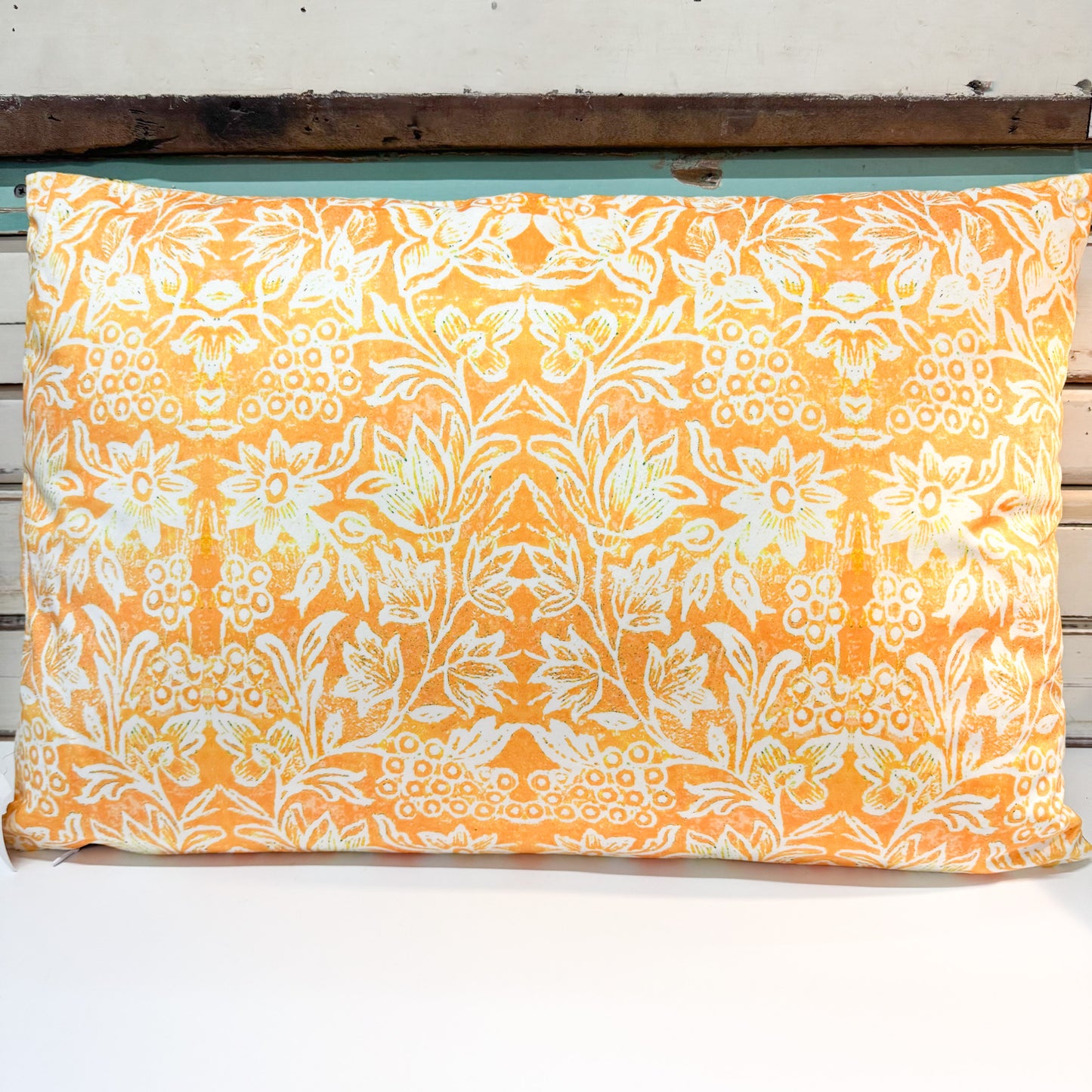 A rectangular decorative pillow with a vibrant orange and white floral damask pattern, resting on a rustic white wooden bench.