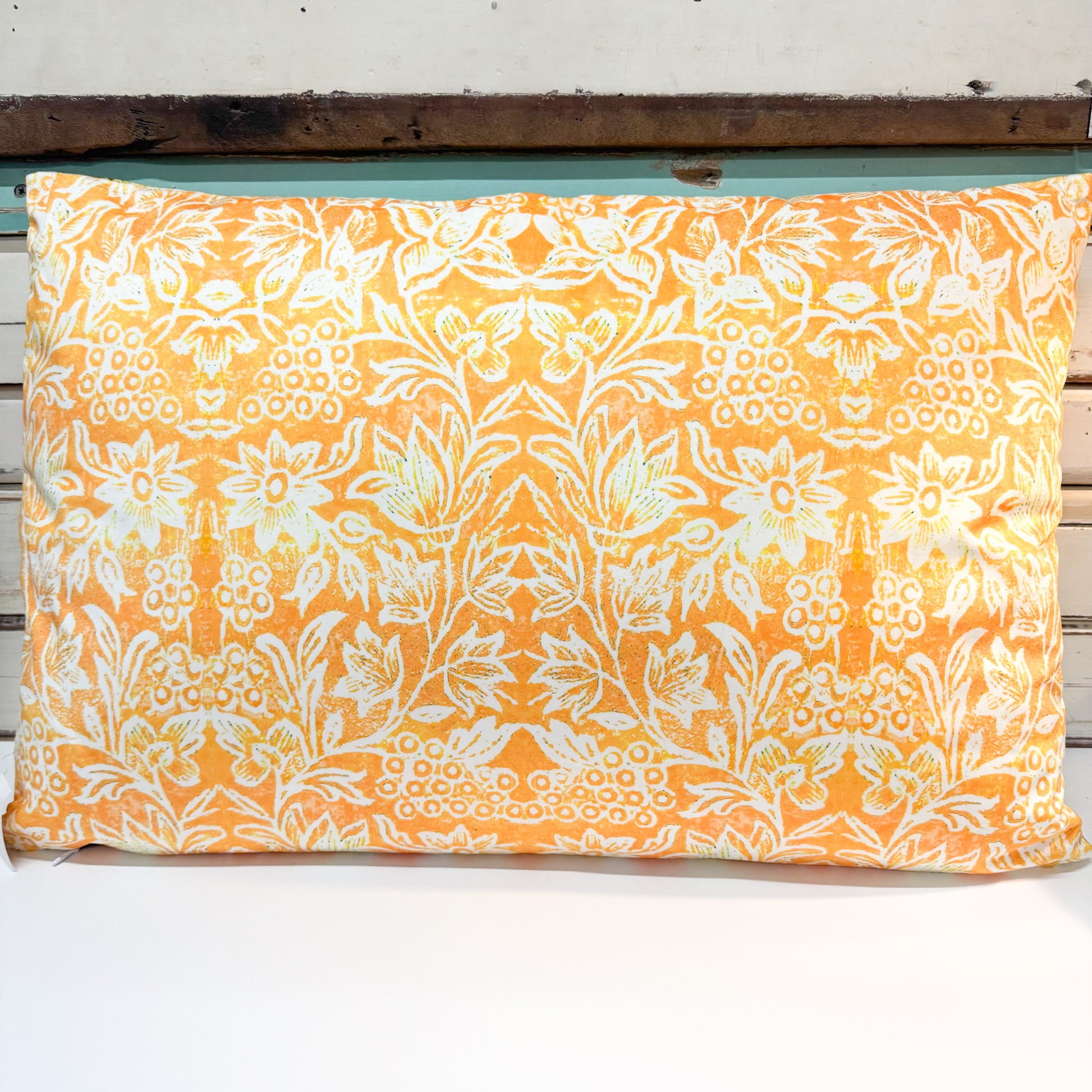 A rectangular decorative pillow with a vibrant orange and white floral damask pattern, resting on a rustic white wooden bench.