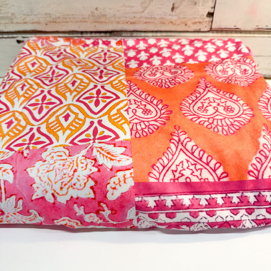 A folded fabric item, likely a blanket or quilt, featuring a split design of two distinct block-print patterns: a pink and orange geometric diamond motif on the left, and a pink paisley motif on the right, with a matching pink and white patterned border.