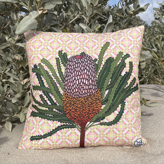 lost and Found art co Banksia 40cm Cushion. Decorative pillow with a floral pattern and central plant design, placed outdoors.