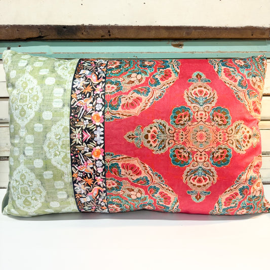 A rectangular decorative throw pillow with a multi-panel fabric design, featuring a red central panel with a teal and gold damask pattern, a green left panel with white floral motifs, and a narrow black floral border stripe.