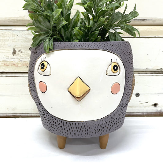 A purple planter designed to resemble a bird's face, with a plant growing out of it. Allen Designs | Birdie Purple Planter