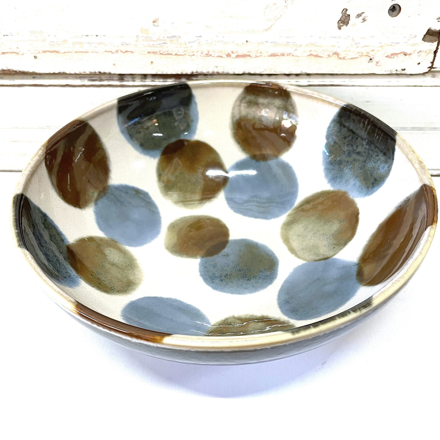 A Japanese ceramic bowl with handpainted blue and brown spots on a semi-gloss glaze, placed on a white surface.