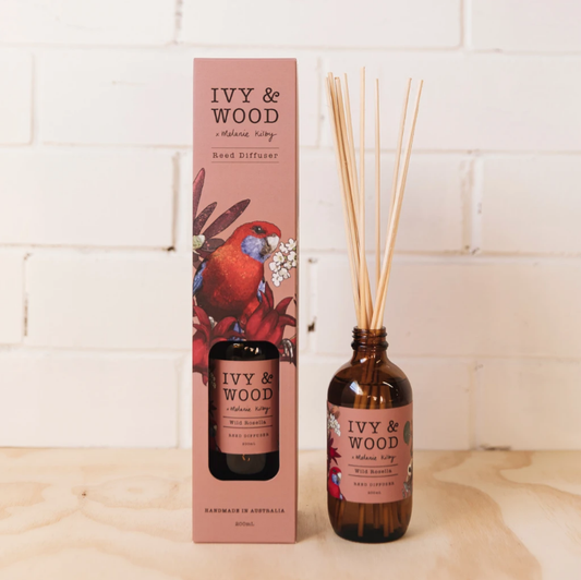 A reed diffuser with amber glass bottle and rattan reeds, labeled 'IVY & WOOD', in front of its packaging box with a floral design and a bird illustration. Ivy & Wood - Wild Rosella Diffuser