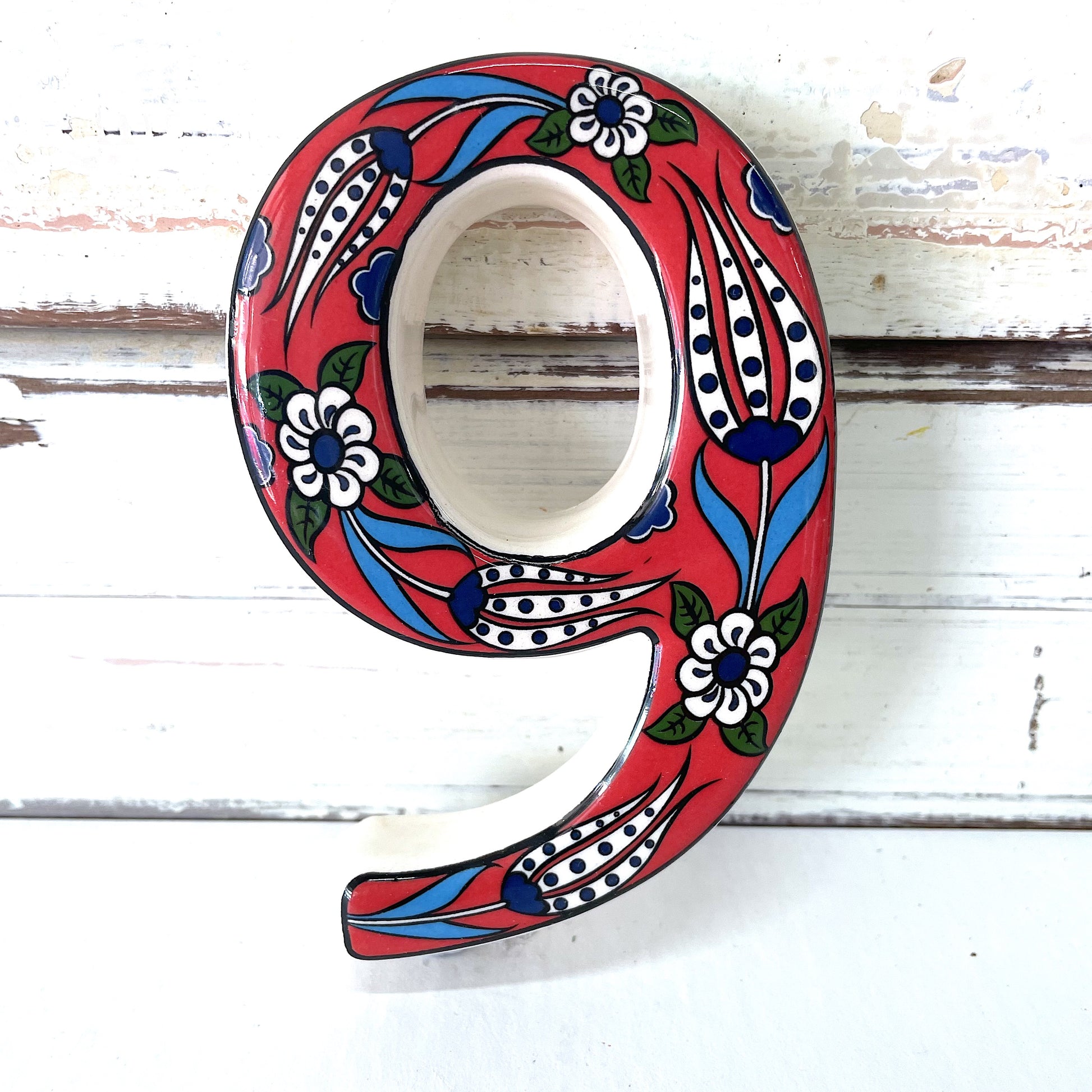A ceramic house number 9 with a red background and floral patterns,