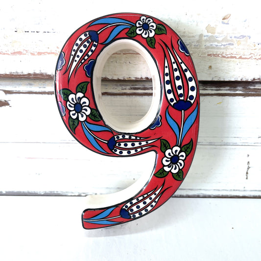A ceramic house number 9 with a red background and floral patterns,