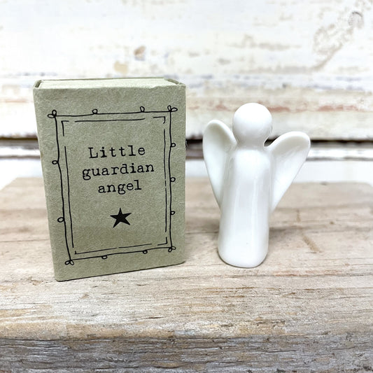 A white porcelain figurine of a little guardian angel sitting on a matchbox box with the text 'Little Guardian Angel' written on it.